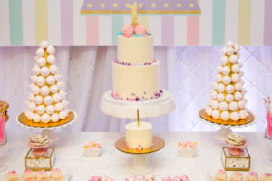 A table setup for a baby girl birthday party showing a cake, sweets and treats